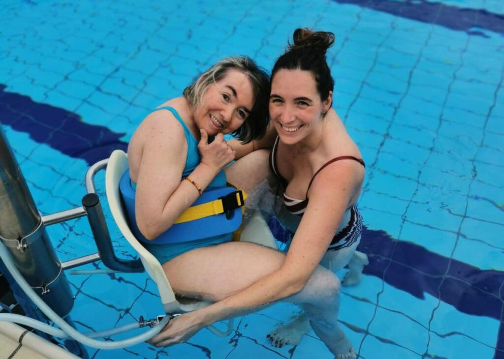 Fabi en la piscina con su fisio Bea. Está sonriente.