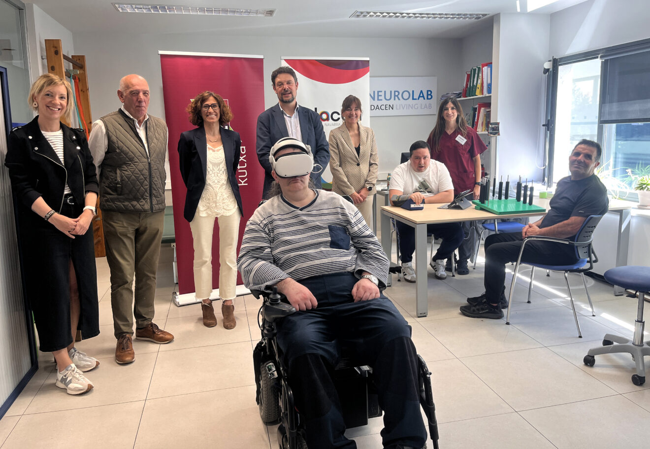 En la imagen se ve a dos resprentantes de LABORAL Kutxa y a varias personas de Adacen, incluidas tres usuarios, en la sala de terapias. Uno de los usuarios lleva las gafas de realidad virtual